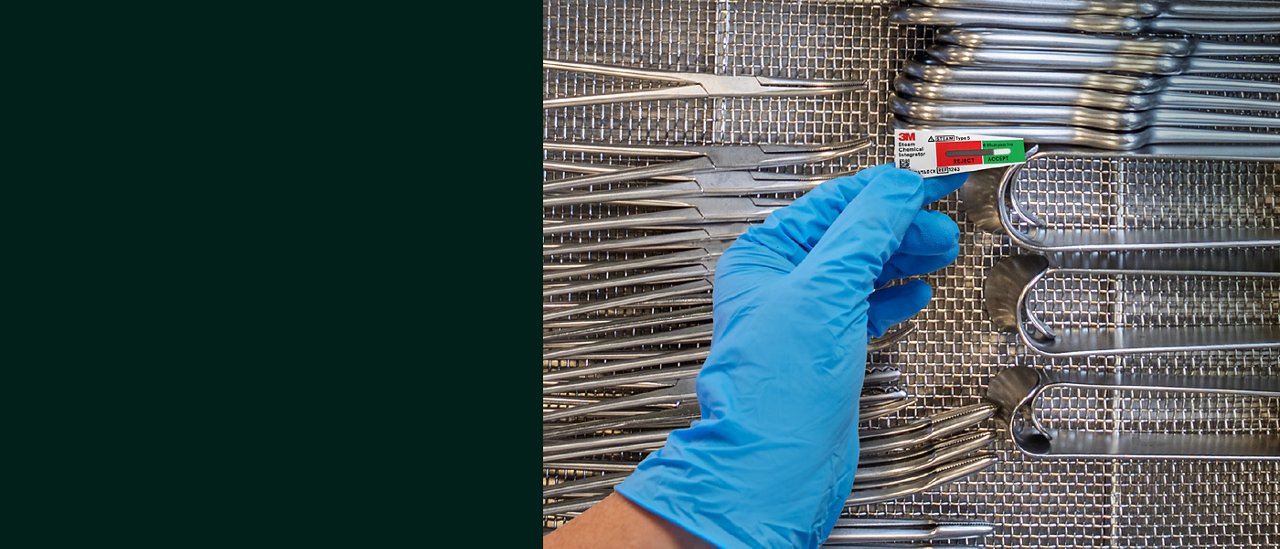 A blue gloved hand is holding a processed 3M™ Attest™ Chemical Indicator above a tray of surgical instruments.